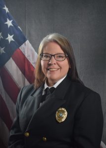 Photo of Jennifer Bossi in Class A uniform in front of draped American Flag