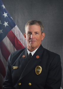 Portrait of Steve Lennon in a Class A uniform in front of an American flag backdrop