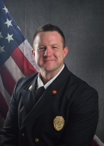 Portrait of Aaron Stritenberger in Class A uniform in front of American flag backdrop