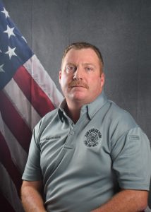 Portrait of Commissioner Tokarz in Class A uniform in front of American flag backdrop