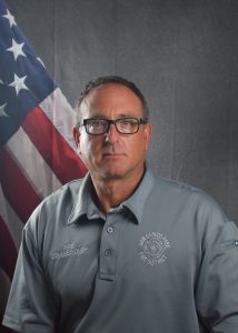 Portrait of Commissioner Wienbaum in Class A uniform in front of American flag backdrop