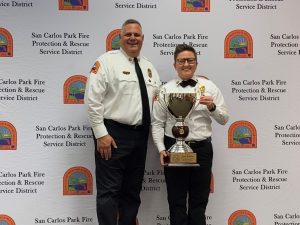 Fire Chief Cambareri and Alexis McLellan posing in front of step and repeat banner with trophy